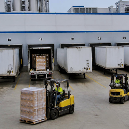 Warehouse loading dock with forklifts moving freight between trailers